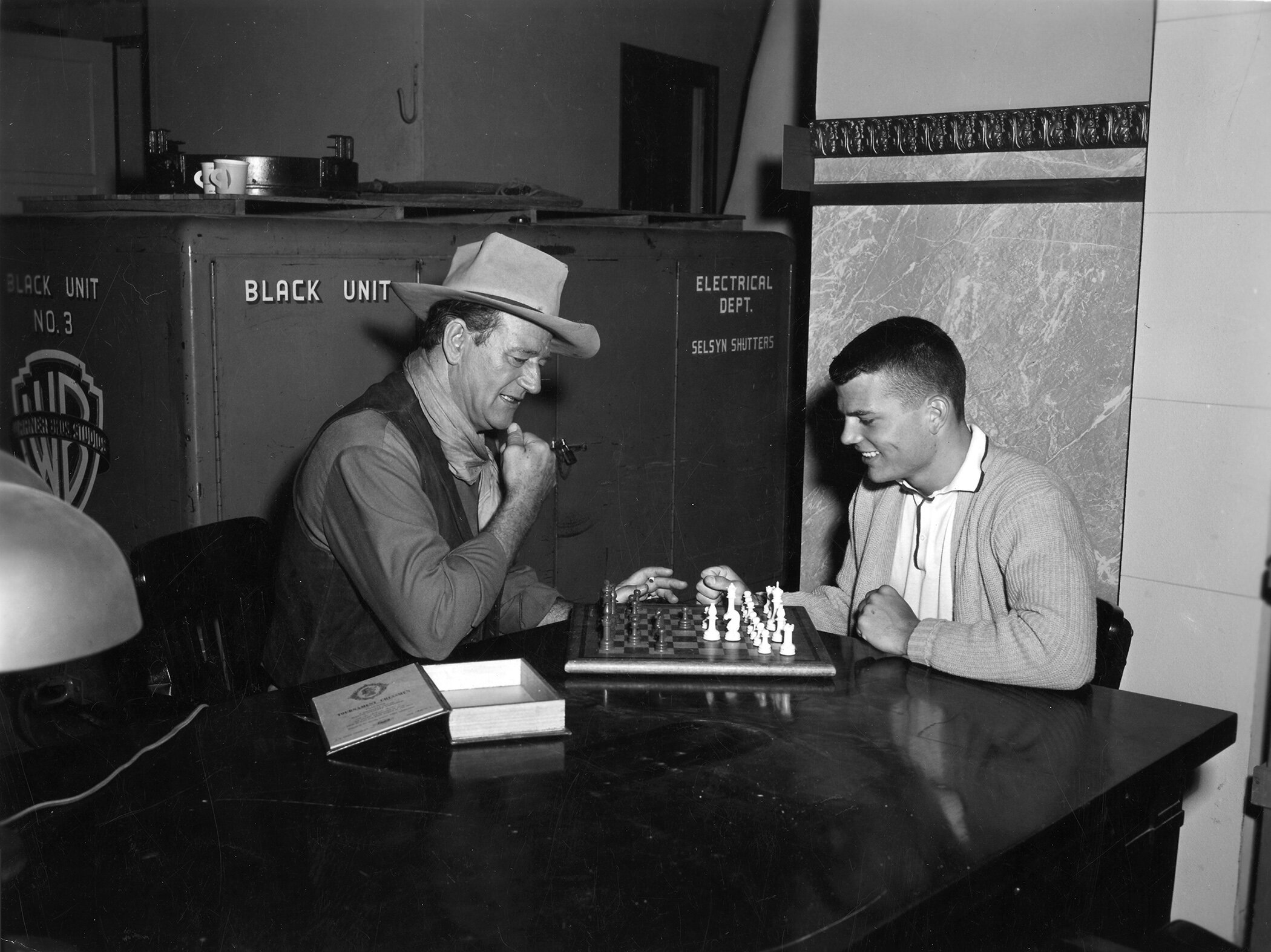 Patrick joins Duke in a game of chess around the time Rio Bravo was filmed. Here, John Wayne wears his signature neckerchief, vest, and cowboy hat often seen in his western films.